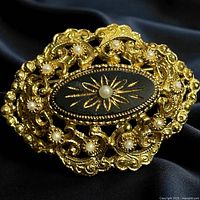 Front view of gold-tone filigree brooch showing black enamel center and seed pearls
