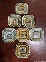 Front view of seven Wade Scotland ashtrays showing central scenes and glazes