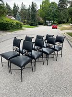 Eight black wrought iron chairs arranged on street, side angle