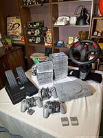 Full lot view showing console, wheel, pedals, controllers, memory cards, and large stack of games