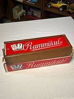 Wooden Rummikub case with red lid on top of original cardboard sleeve