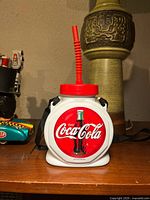 Front view of Coca-Cola plastic canteen showing lid, straw, logo and strap