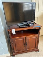 TV resting on top of wood cabinet with remotes and cables visible