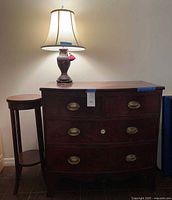 Front view of dresser with lamp on top and plant stand beside it