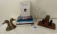 overview of lot: brass duck bookends, wood bookends, glass carafe, stack of seven decoy books