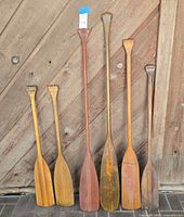 Front view of six wooden paddles leaning against wood wall