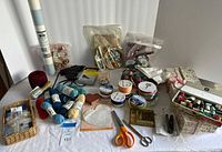 Overall view of all craft items on table including yarn, threads, ribbons, glue gun, scissors, buttons, lace, York roll, stamp box