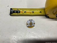 Front view of enamel Bruins jersey pin beside ruler showing roughly 1.25-inch width