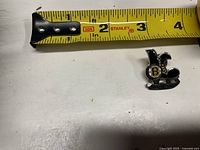 Skate-shaped Boston Bruins enamel pin beside tape measure showing ~1-inch length
