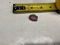 Front view of Montreal Canadiens enamel lapel pin beside ruler showing ~1-in. width