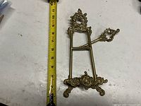 Front view of brass easel next to tape measure