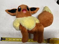 Front view of Eevee plush beside tape measure showing about 12-inch length