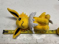Full view of Jolteon plush beside tape measure showing length