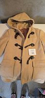 Full view of tan duffle coat showing hood, pockets, toggles