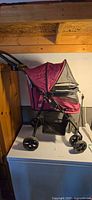 Side view of maroon Pet Gear cat stroller showing wheels and basket