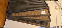 Stack of four floor mats showing black rubber tray, brown coir mat, and other two mats