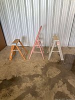 Three ladders standing: wood, pink hook, aluminum step
