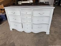Front view showing nine drawers, serpentine front, carved details, white paint, gray top