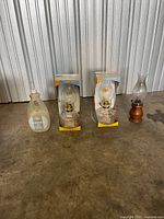 Group shot of lamp oil bottle, two boxed oil lamps, one unboxed oil lamp