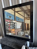 Mirror reflection shows round glass coffee table, grey armless chair, wicker basket