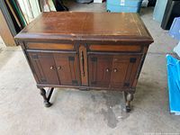 Front view of dark stained record cabinet showing two paneled doors, hardware, turned legs, stretcher base, and top surface wear