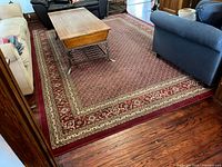 Full view of rug showing red field, beige floral border, surrounding furniture for scale