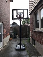 Full view of basketball hoop in driveway including base, pole, backboard, and rim