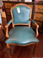 Front view of teal vinyl armchair showing seat wear and nailhead trim