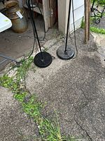 Bases of both black metal floor lamps on driveway