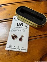 Stud earrings, pendant, and metal tin on wooden surface