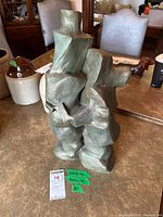 Front view of green patinated abstract clay sculpture with signature tag visible