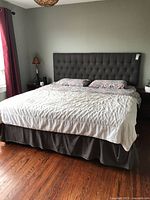Full view of king bed with headboard, bedding, mattress on hardwood floor
