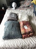 All four folded sheet sets on bed: teal print, rust paisley, dark grey, ivory