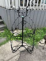 Full front view of black wrought iron six-tier plant stand outdoors