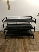 Full frontal view of three-tier black steel and plastic shoe rack