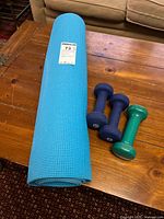 Rolled blue yoga mat beside three dumbbells on wooden table