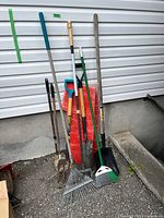 Group of long-handled yard tools leaning against wall