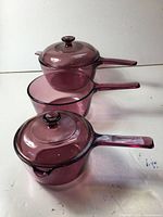 Three cranberry glass saucepans in nesting order, two with lids