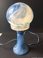 Full view of lamp lit, showing globe shade, pedestal base, blue cord