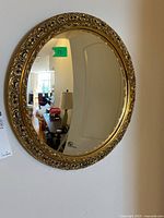 Full view of round mirror with gold ornate frame mounted on wall