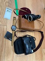 All items together: Timex watch, binoculars in leather case, Canon camera with pouch, burgundy round case