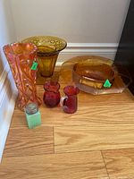Group shot: tall carnival vase, golden vase with frog, amber bowl, two cranberry pitchers, green shaker