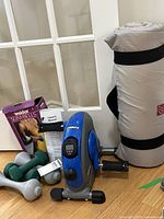 Stamina pedal exerciser, Bally mat rolled, Weider Slim Bells box, grey and green dumbbells