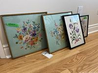 Four framed needlepoint artworks leaning against wall