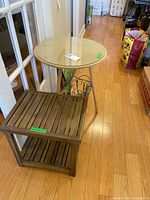 round glass-top side table next to wood slat table with magazine rack visible