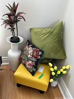 Group view showing yellow stool, green pillow, floral pillow, white vase with plant, glass vase with tulips