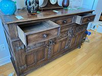 Front view of carved wood sideboard showing drawers, doors, carvings, and hardware