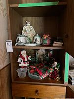 Cabinet shelf showing majority of items including brass candlesticks, ceramic pieces, plates, napkins, ornaments