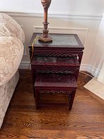 Set of three oriental style nesting tables stacked, showing carved details and glass top on largest table