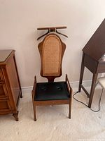 Front view of valet chair showing cane back, black seat, hanger bar and shelf